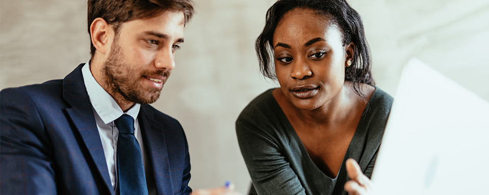 Eine dunkelhaarige Frau und ein Mann im blauen Anzug informieren sich am Laptop über den sicheren Messenger Netsfere