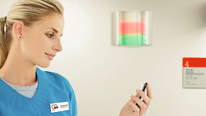 Eine Mitarbeiterin des AWO Bezirksverband Schwaben e.V. steht vor einer Lichtrufanlage und schaut auf ihr Mobiltelefon