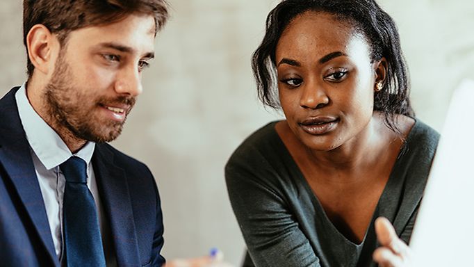 Eine dunkelhaarige Frau und ein Mann im blauen Anzug informieren sich am Laptop über den sicheren Messenger Netsfere