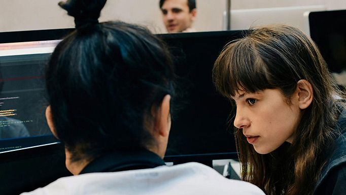 Digitales Krisenhandbuch öffentliche Betriebe: Zwei Frauen in einem Rechenzentrum vor mehreren Bildschirmen unterhalten sich