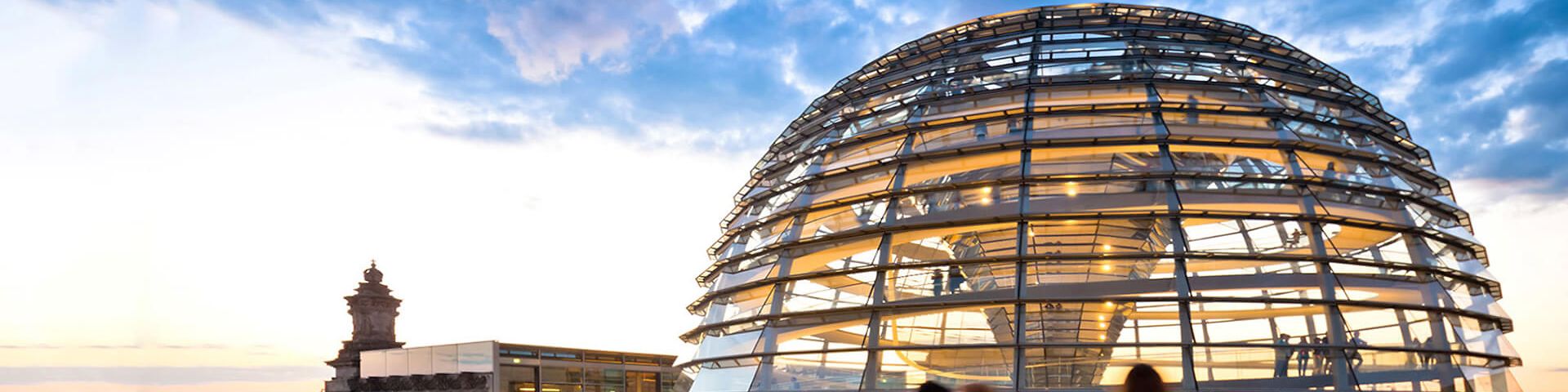 Die Bundestagsglaskuppel in den Wolken von Berlin, davor gehen Menschen
