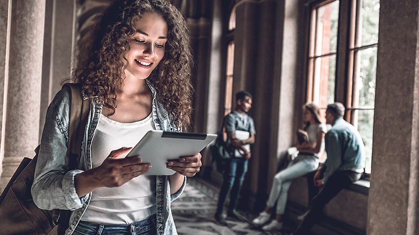 Breitbandanschluss Schule: Studierende im Campusgebäude schaut lächelnd auf ein Tablet 