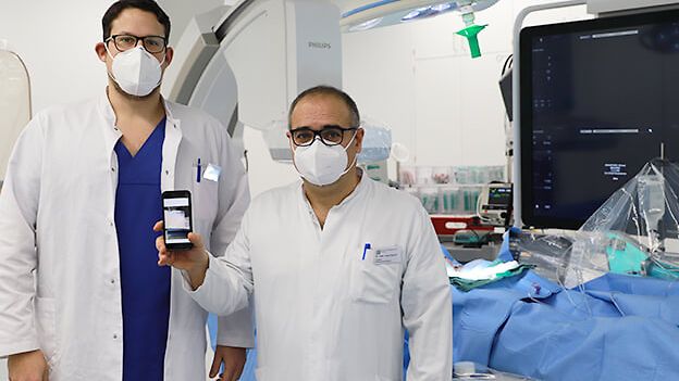 Zwei Ärzte im Krankenzimmer halten ein Handy hoch