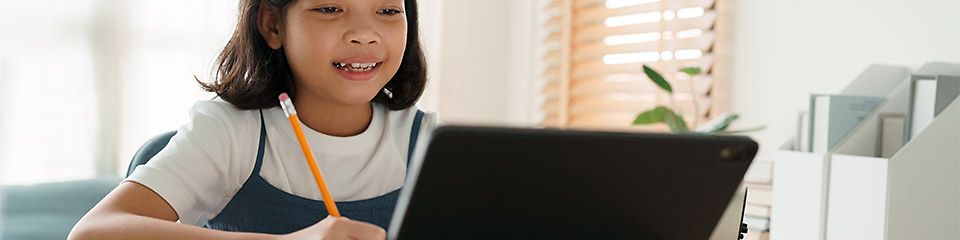 Samsung Hardware: Schülerin sitzt mit Bleistift am Schreibtisch und schaut lächelnd auf ihr Tablet 
