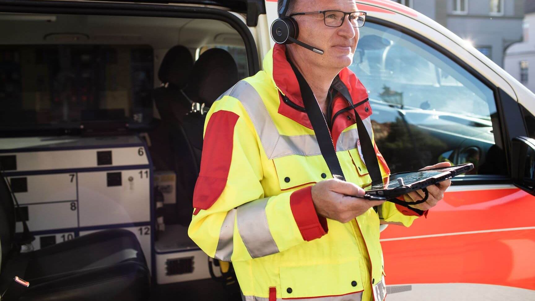 Digitale Rettungswagen Ausstattung: Ein ärztlicher Notfallhelfer steht mit einem Tablet vor seinem Einsatzfahrzeug