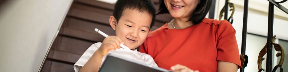 Eine Mutter und ihr Sohn lernen gemeinsam am Tablet mithilfe von Apple Bildung und lächeln dabei