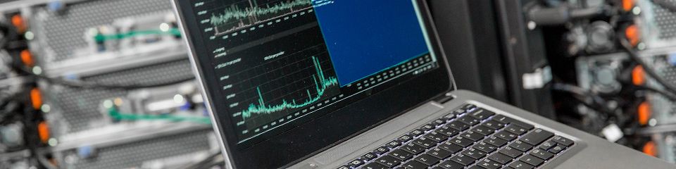 Ein Laptop mit Diagnosebildschirm im Rahmen einer IT-Netzwerkanalyse im öffentlichen Sektor, im Hintergrund undeutlich ein Server-Rack mit Kabeln