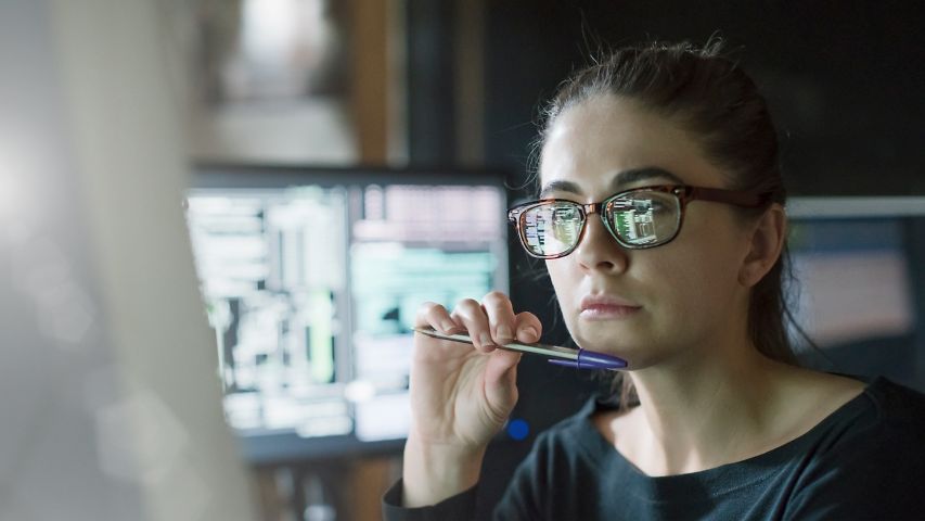 Mehrere Personen blicken in einem Konferenzraum auf einen Bildschirm, auf dem ein Teamscall läuft