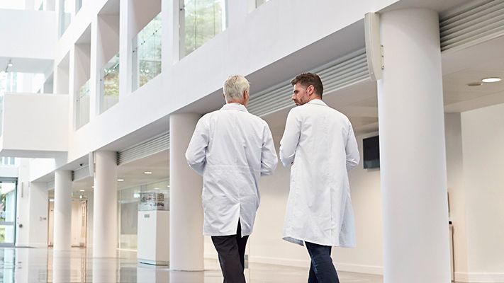 zwei herren in weißem kittel laufen durch ein helles foyer