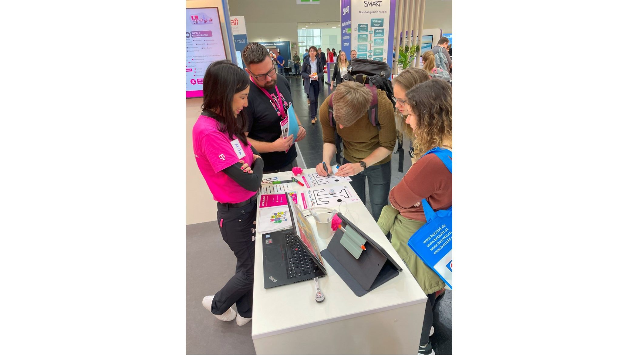 Menschen interagieren an einem Messestand, begleitet von einer Mitarbeiterin in Magenta