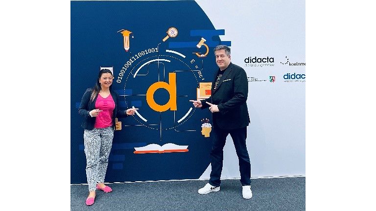 Julia und Andreas stehen vor einem didacta-Messe-Logo