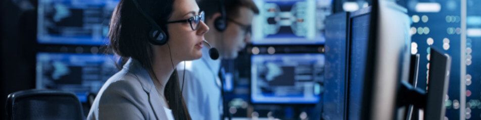 IT-Fachkräfte in einem Kontrollzentrum mit Headsets vor Monitoren und Datenvisualisierungen