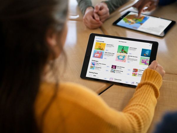 Schülerin nutzt ein Tablet im Unterricht, während weitere Geräte im Hintergrund verwendet werden.