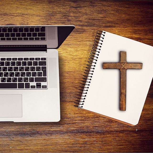 Laptop neben Notizbuch mit Holzkreuz auf Holztisch