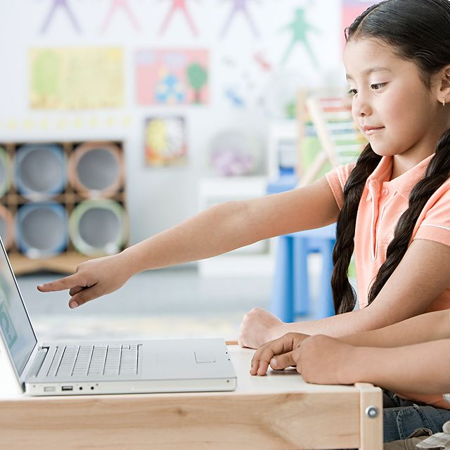 Zwei Kinder arbeiten im Klassenzimmer gemeinsam an einem Laptop, ein Mädchen zeigt auf den Bildschirm.