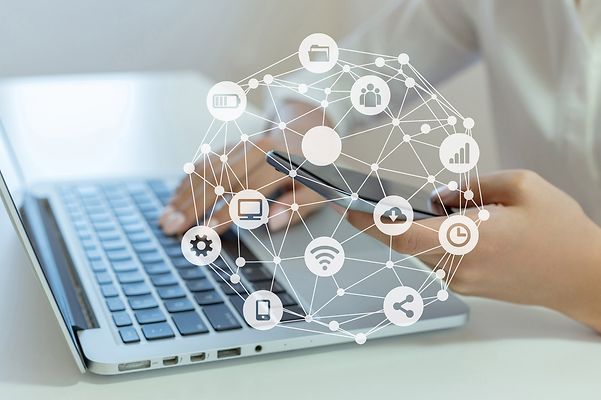 Hände bedienen Laptop und Smartphone, darüber digitale vernetzte Symbole