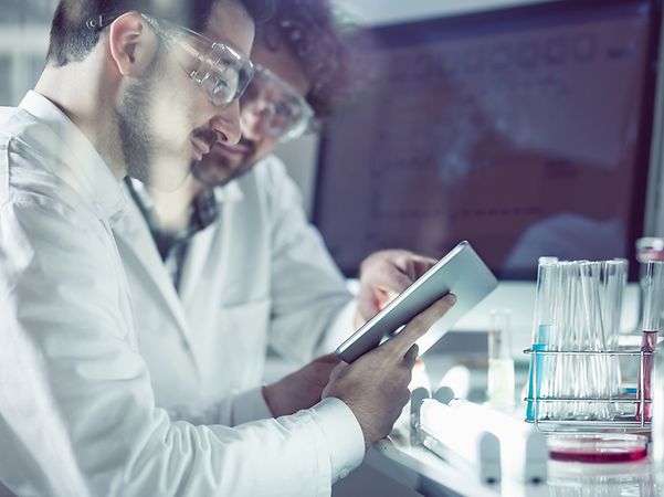 Personen im Labor betrachten ein Tablet neben Laborgeräten und Probenröhrchen