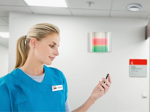A hospital nurse is looking at a mobile device in the corridor.