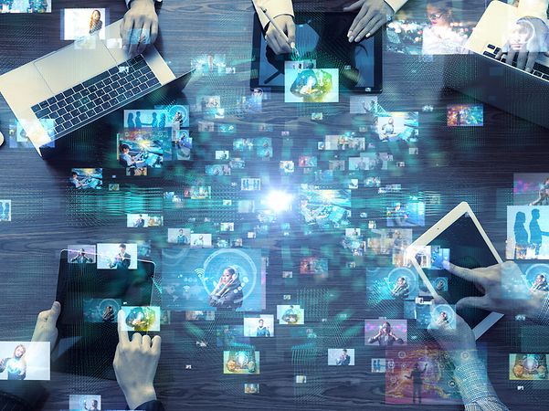 Digitale Geräte auf einem Tisch mit darüber eingeblendeten Symbolen für vernetzte Datenflüsse.