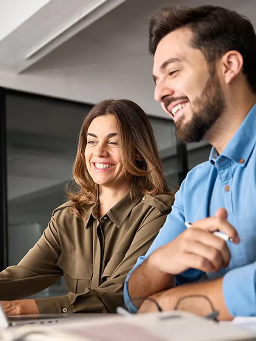 Zwei Personen arbeiten mit SAP®-Lösungen der T-Systems und sitzen lächelnd vor einem Laptop im Büro.