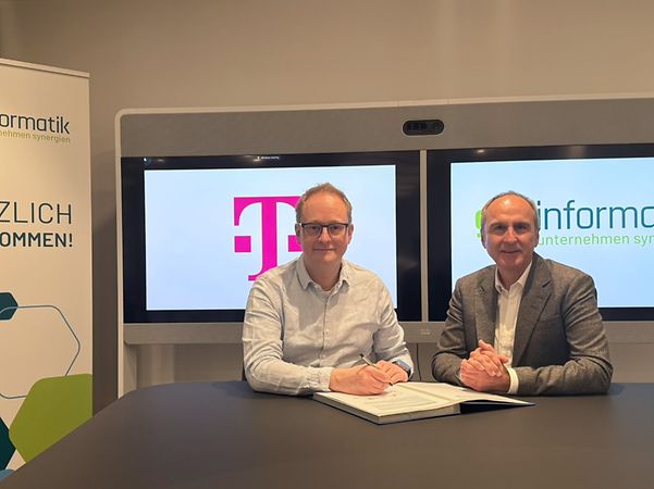 Zwei Männer sitzen vor gkv-informatik- und Telekom-Displays.