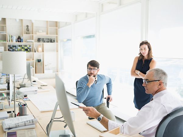 Drei Personen besprechen sich in einem hellen Büro an einem Computer.