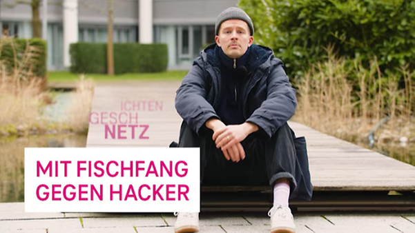 Person auf Holzplattform mit Schild „Mit Fischfang gegen Hacker“, Video-Vorschaubild im Außenbereich.