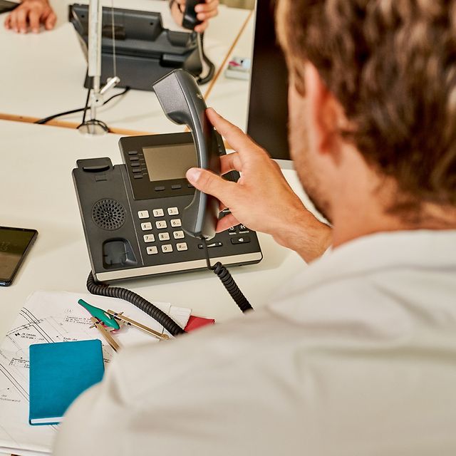 Person bedient ein Festnetztelefon am Schreibtisch.