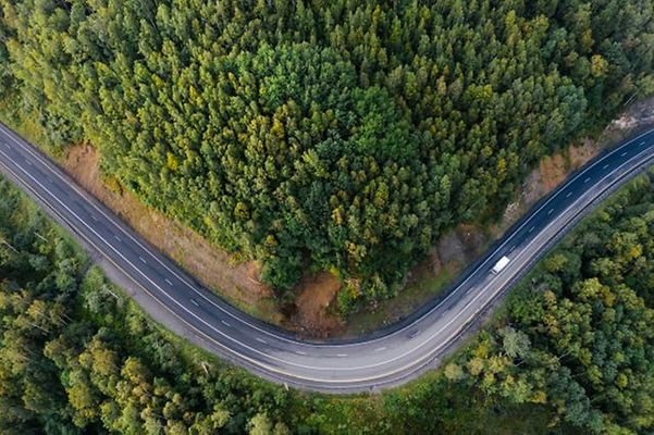 A drone shot of a winding road through dense woodland, featuring a vehicle.