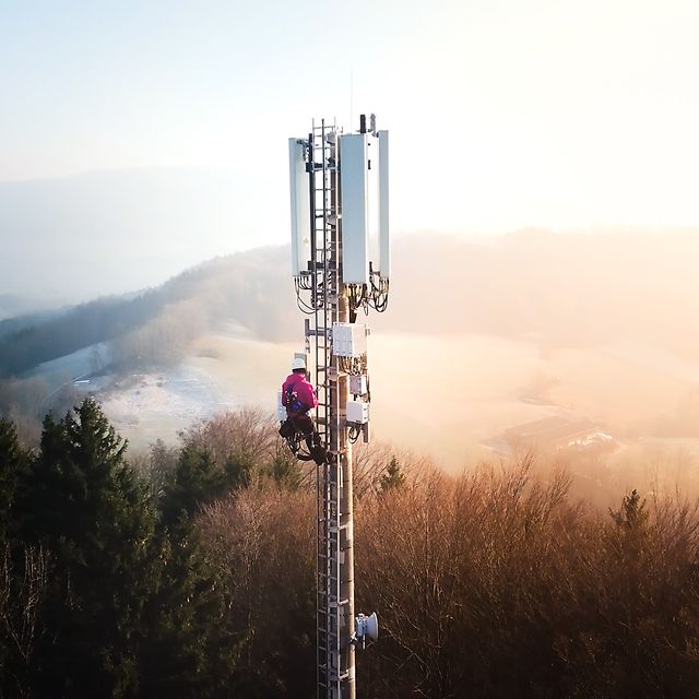 A technician is working on a mobile phone mast in a hilly landscape