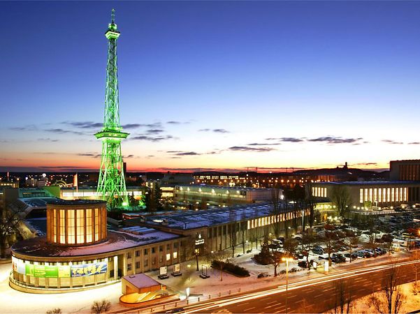 The Berlin Exhibition Grounds, illuminated, with the Radio Tower and surrounding buildings at dusk.