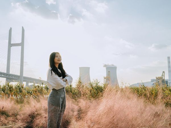 A person is standing in a meadow in front of a factory building that uses energy management