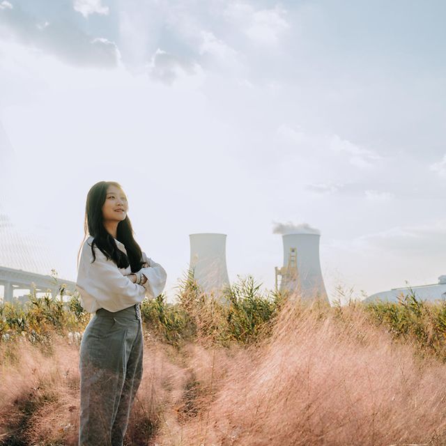 A person is standing in a meadow in front of a factory building that uses energy management