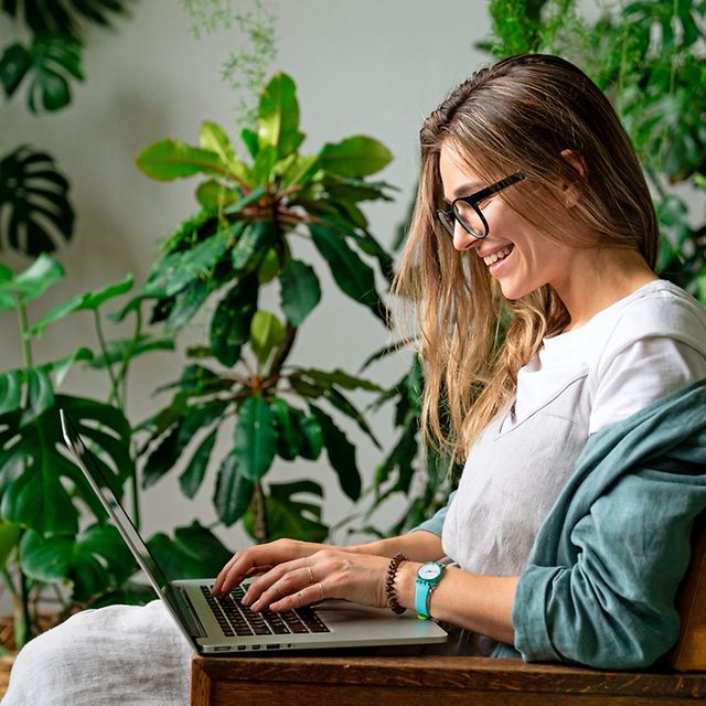 A woman is sitting in a room full of plants with a laptop on her lap