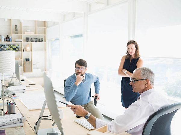 Three people are working together in the office and discussing what is on the screen.