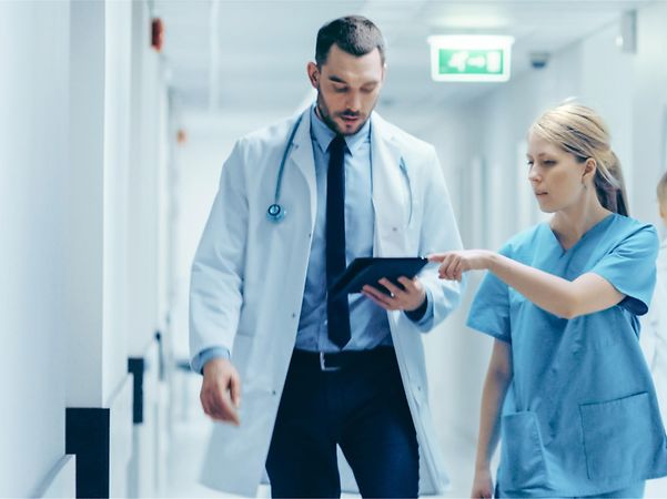 A doctor and a nurse are discussing information together on a tablet in the hospital corridor.