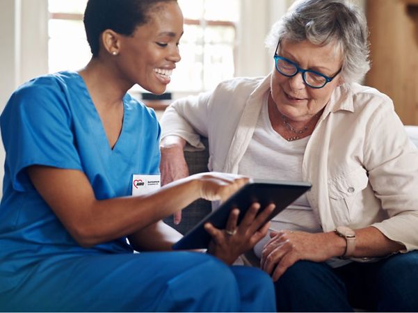 A carer smiles as she shows an elderly woman the contents of a tablet.