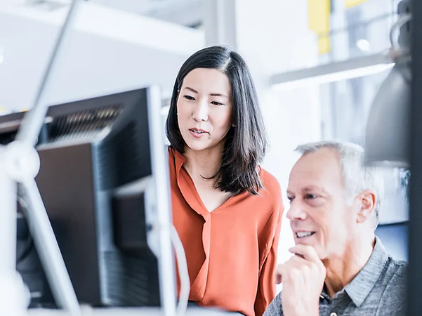 Two people are working together on a desktop computer in the office.