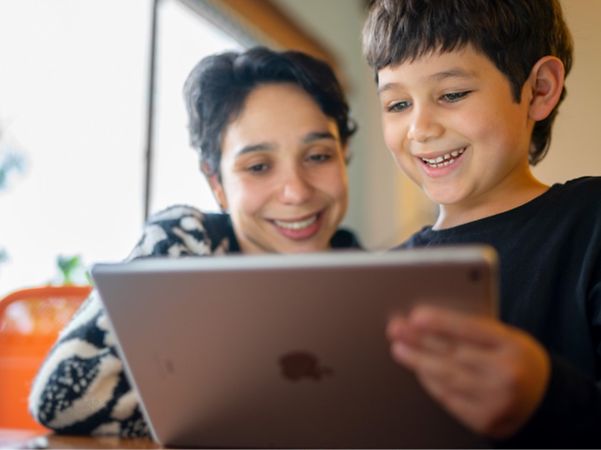 Two children are looking at a tablet together, smiling.