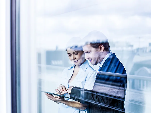 Two people are using a tablet together in front of a glass wall.