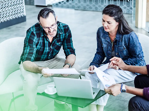 Three people are sitting at a table, working together on their laptops and with their documents
