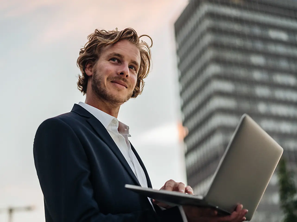 A businessman is working on a laptop in front of a modern office block.