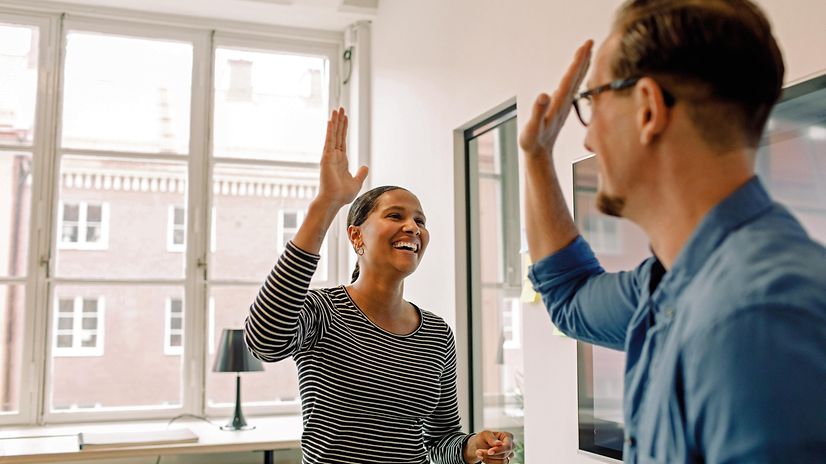 Two people high-five each other in the office after a successful project.