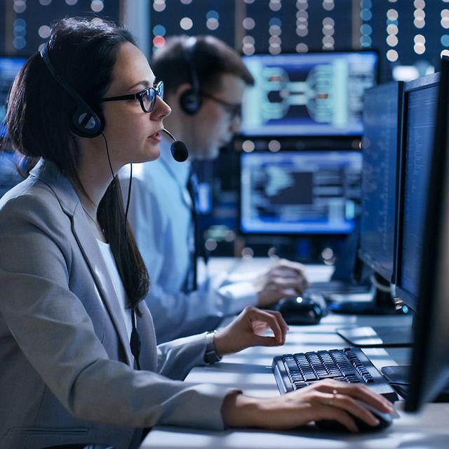 Two employees are sitting in the office wearing headsets and using Telekom's AlarmRuf service