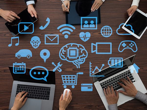 People are working on laptops, surrounded by digital cloud and IT symbols.