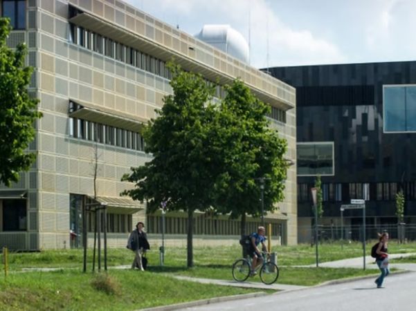 Modern university buildings at the University of Potsdam, with green spaces, trees and cyclists passing by.
