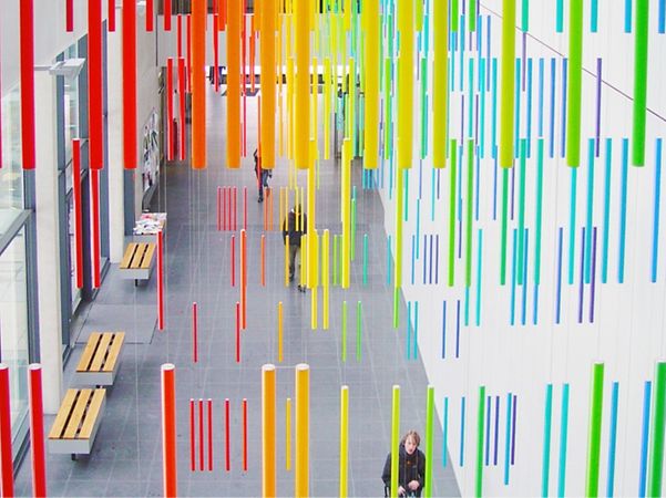 The interior of a modern university building featuring colourful hanging rods and benches.