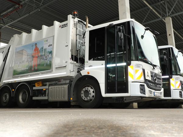 Several refuse collection lorries belonging to the waste management company are parked in a vehicle shed.