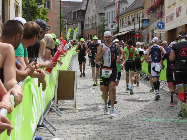 Participants in a running or triathlon event make their way through a city centre, whilst spectators line the route.