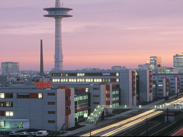 A cityscape of Essen featuring modern buildings, road traffic and the striking television tower at dusk.